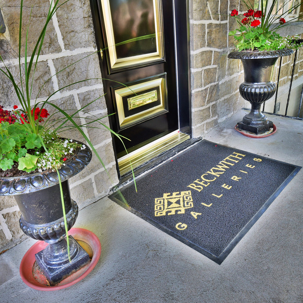 The front door and door mat of Beckwith Galleries' Ottawa location, nestled between two beautiful plants..