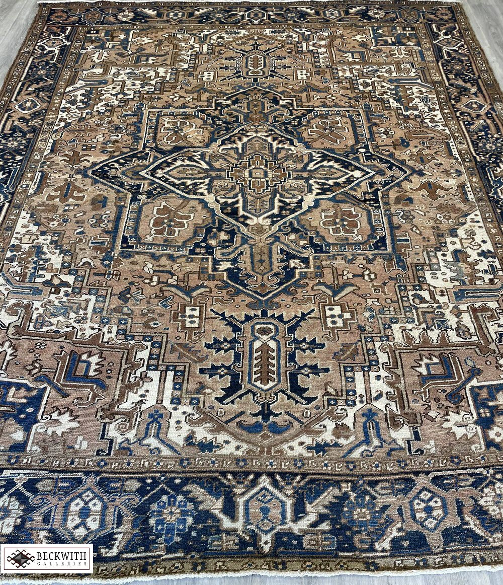 An antique Heriz rug with a geometric pattern in cream, blue, and brown colors, showing signs of wear.