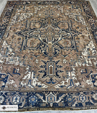 An antique Heriz rug with a geometric pattern in cream, blue, and brown colors, showing signs of wear.