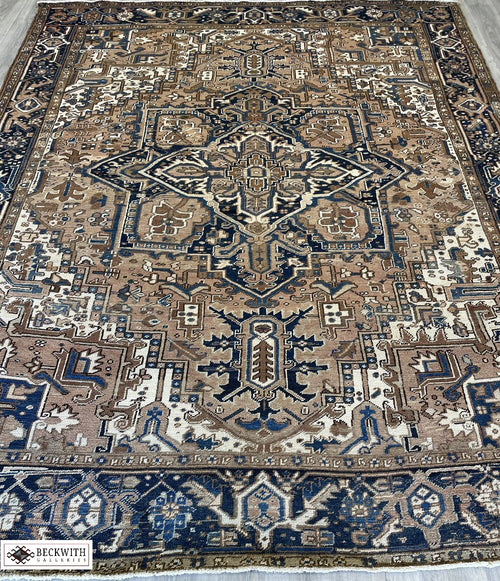 An antique Heriz rug with a geometric pattern in cream, blue, and brown colors, showing signs of wear.