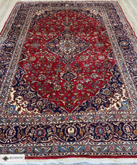 A Kashan-style rug with a floral pattern in blue, red, and gray hues on a white background.