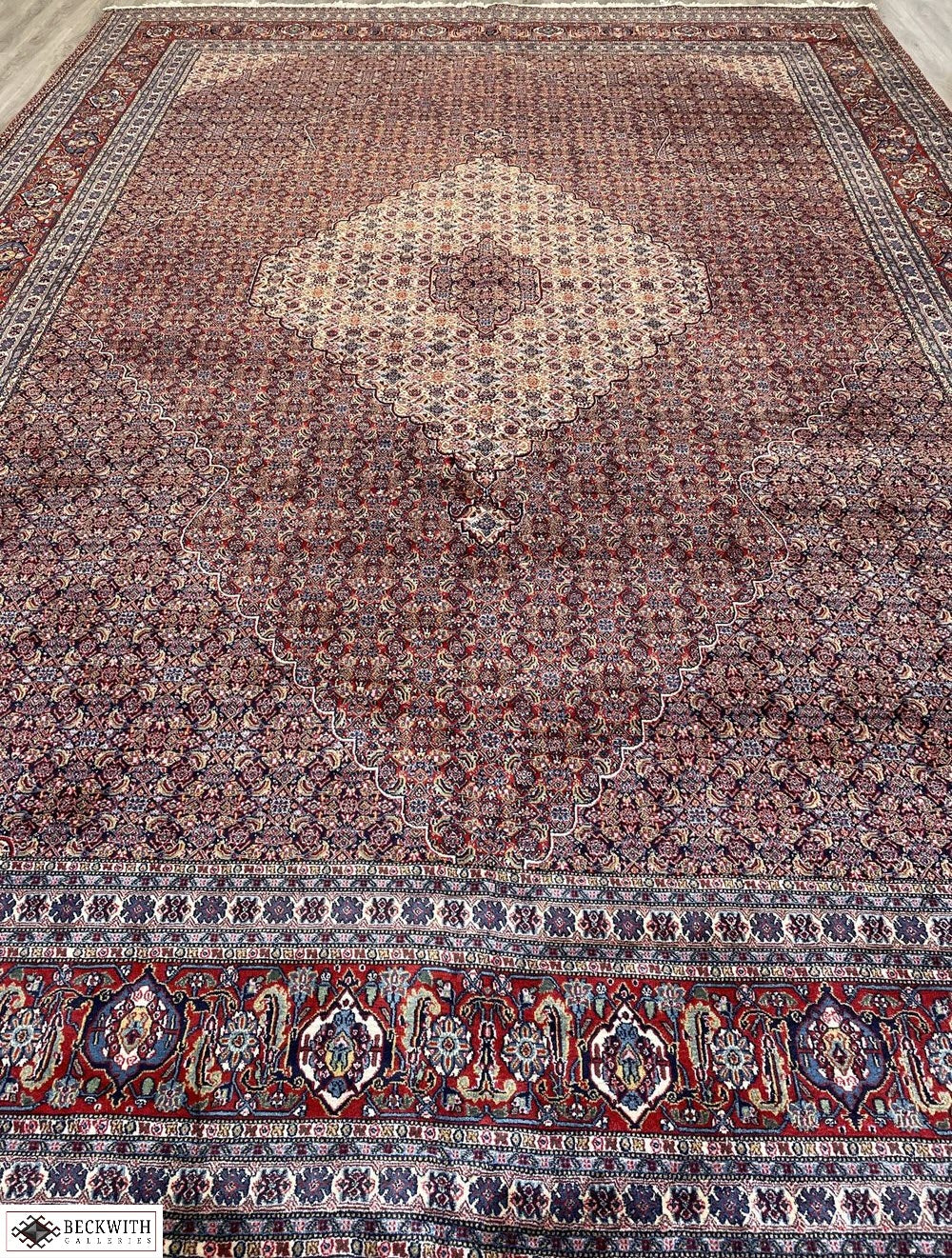 An oversized, hand-knotted Sarab rug with a geometric pattern, predominantly in red and blue colors, showcasing intricate detailing.