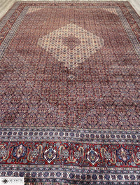An oversized, hand-knotted Sarab rug with a geometric pattern, predominantly in red and blue colors, showcasing intricate detailing.