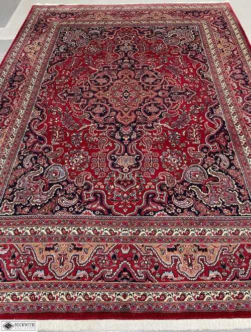 A vintage Mashad rug with a red background and traditional geometric pattern, hand-knotted wool pile on a cotton base.