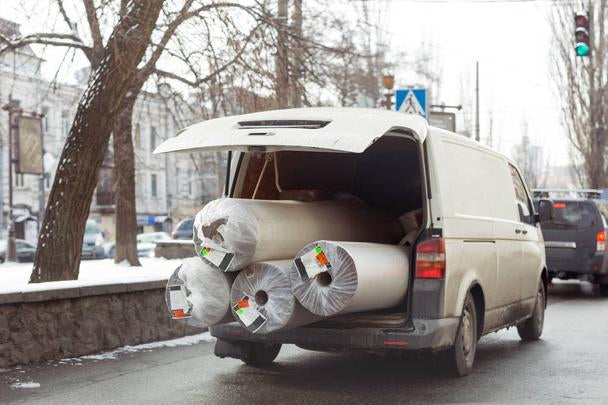 Carpet delivery van with open trunk and rolls of carpets on display.